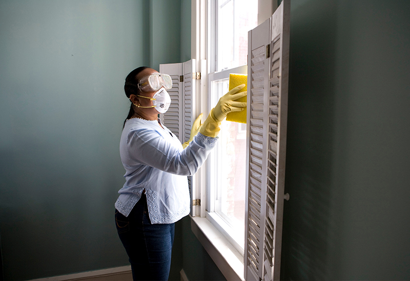 Woman cleaning around windows with goggles and a mask on